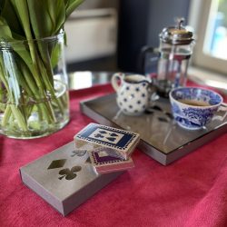 Grey sleeved box with silver gilt playing cards, showing navy and purple designs, with tray and coffee pot and cup in background