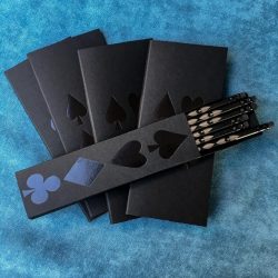 4 black score pads and black box of six pencils on caribbean blue bridge cloth